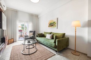 Un salon avec un canapé vert, une table basse ronde, une lampe et un tableau accroché au mur.