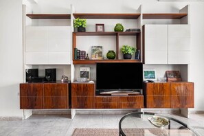 Un salon moderne doté d’un téléviseur à écran plat, de meubles en bois et d’étagères ornées d’objets décoratifs.