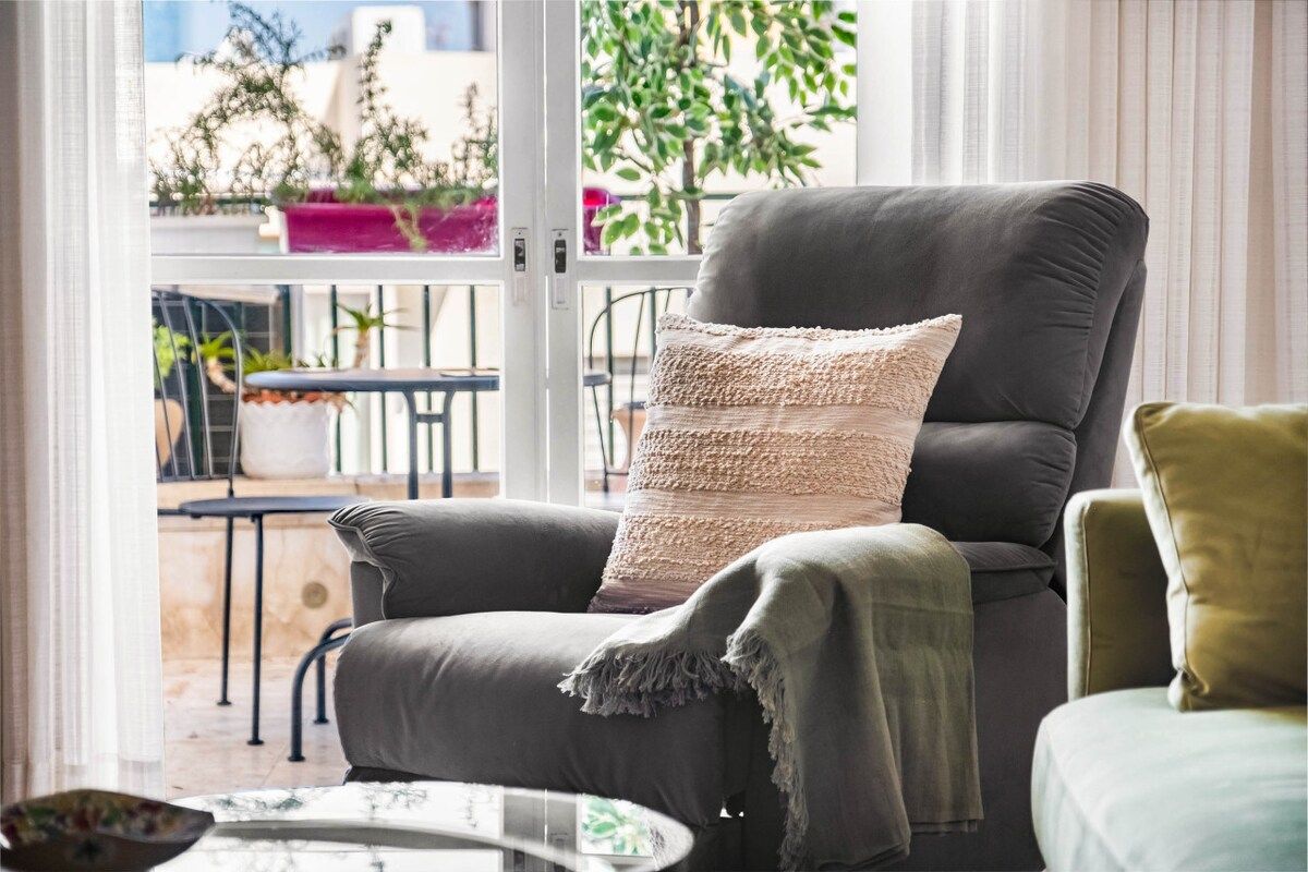 A modern living room with a grey sofa, a woven throw pillow, and a green throw blanket.