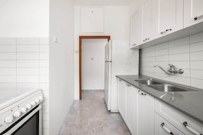 Una cocina con armarios blancos, un lavamanos de acero inoxidable y una estufa.