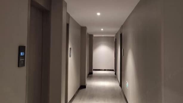 Un long couloir étroit, doté d’un sol et de murs aux couleurs claires, qui mène à un espace lumineux à son extrémité.