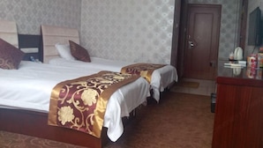 Une chambre d’hôtel avec un grand lit, deux petits lits, une commode en bois et une porte donnant sur une autre pièce.