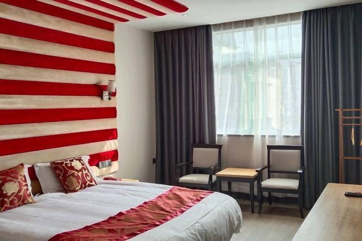 Une chambre d’hôtel avec un lit, deux chaises, une petite table et une fenêtre avec des rideaux.
