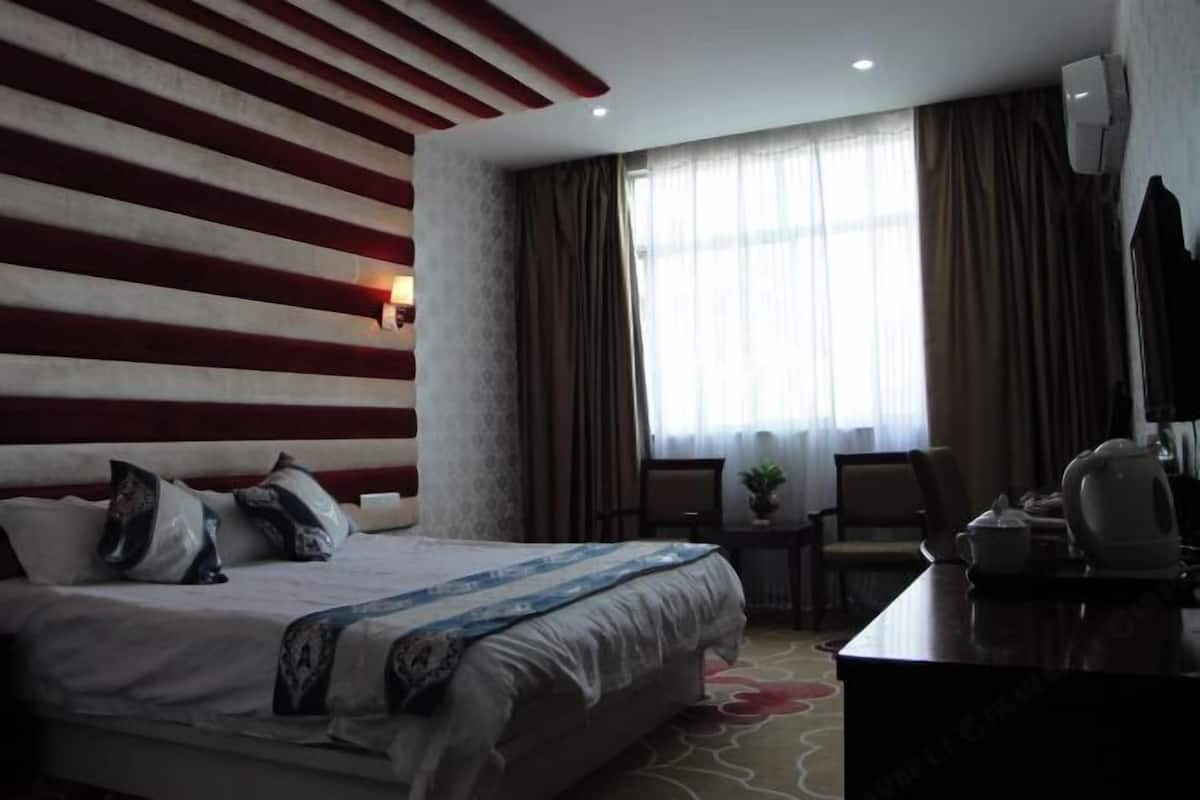 Une chambre d’hôtel avec un grand lit, un bureau avec une bouilloire et une fenêtre avec des rideaux.