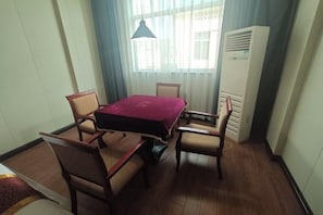 A hotel room with a dining table, four chairs, a bed, a window with curtains, and a standing heater. - Gongxiao Hotel (Kaihua)