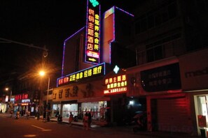 A building with illuminated signage, a street in front, and a few pedestrians. - Gongxiao Hotel (Kaihua)