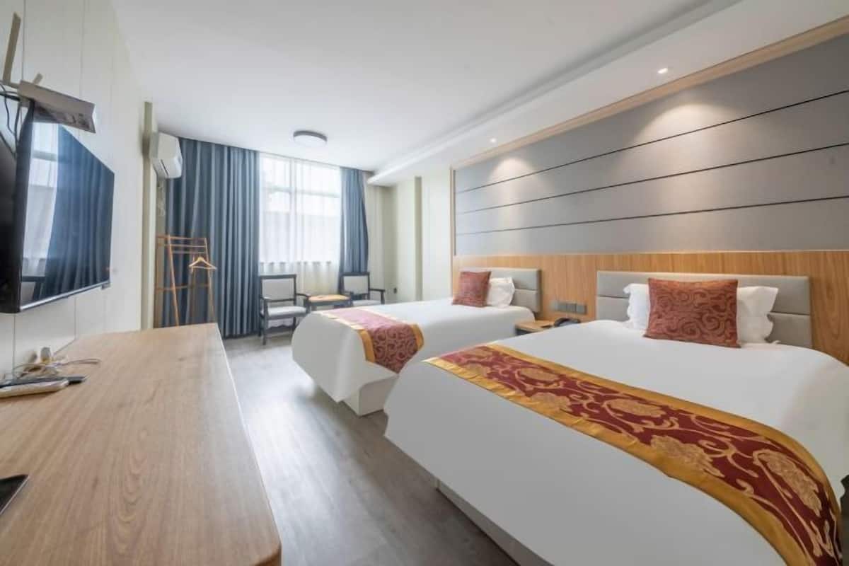 Une chambre d’hôtel avec deux lits, un bureau en bois, un téléviseur à écran plat et une grande fenêtre avec des rideaux.