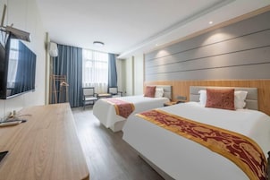 Habitación de hotel con dos camas, un escritorio de madera, un televisor de pantalla plana y un ventanal con cortinas.