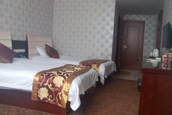 A hotel room with two beds, a wooden headboard, a wardrobe, and a door leading to another room.