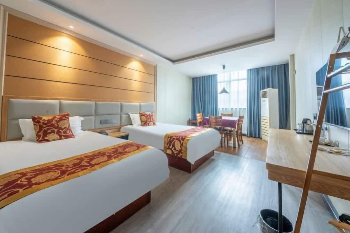 Une chambre d’hôtel avec deux lits, un bureau, une chaise et une fenêtre avec des rideaux.