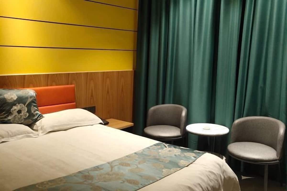 Une chambre d’hôtel avec un lit, deux chaises, une petite table et un rideau.