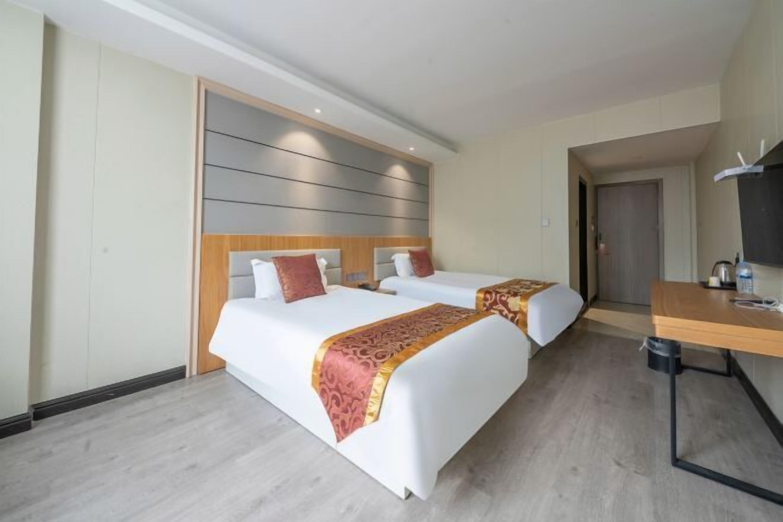 A hotel room with two beds, a wooden headboard, a desk with a chair, and a television.