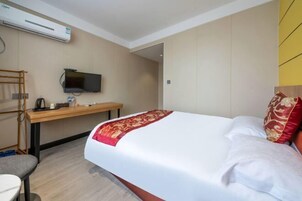 Una habitación de hotel con cama, escritorio, televisor y aire acondicionado.