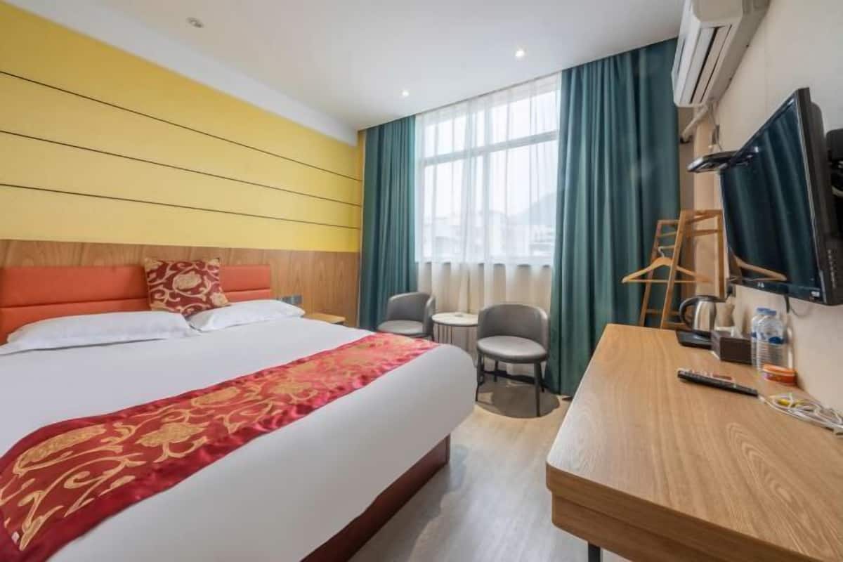 Une chambre d’hôtel avec un grand lit, un bureau, une chaise, une télévision et une fenêtre avec des rideaux.