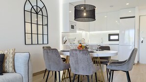 Una cocina moderna con armarios blancos, una mesa redonda de comedor con sillas tapizadas en gris y una lámpara colgante.