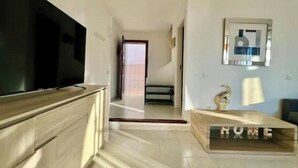 Un salon spacieux avec un grand téléviseur à écran plat, une table basse en bois et un panneau décoratif portant l’inscription « HOME ».