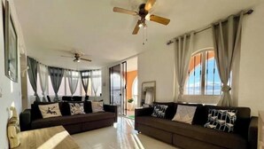 Un salon spacieux avec deux canapés sombres, une table basse en bois et un ventilateur de plafond.