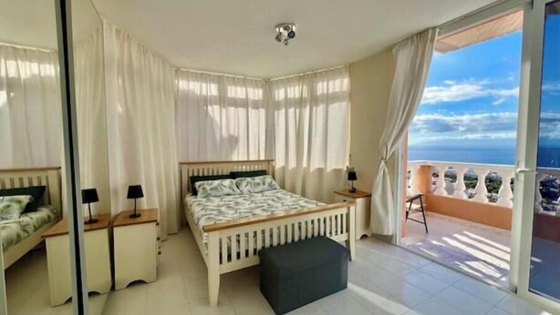 Une chambre à coucher avec un lit, des tables de chevet, un petit canapé et un balcon donnant sur la mer.