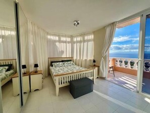 Un dormitorio con cama, mesitas de noche, un pequeño sofá y un balcón con vista al mar.