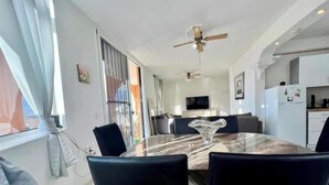 Un coin repas avec une table en marbre, des chaises noires, un ventilateur de plafond et une cuisine en arrière-plan.