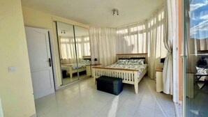 Une chambre à coucher avec un lit, un miroir, une porte-fenêtre coulissante et un sol carrelé.