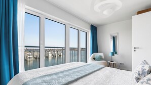 A modern hotel room with a large bed, a view of a marina, and a cityscape.