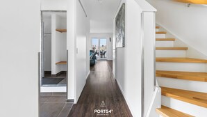 A modern hallway with a wooden staircase, a view into a living area, and a door leading to another room.