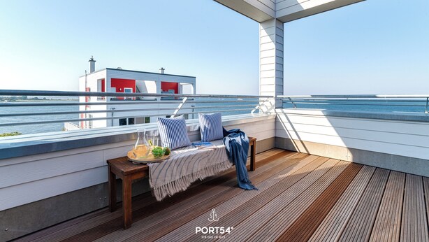 A deck with a bench, a table with a drink and fruit, and a view of a building with a red door.