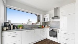 A modern kitchen with white cabinets, a stainless steel range, and a large window overlooking a garden.