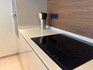 A modern kitchen with a built-in induction cooktop, a wooden backsplash, and a minimalist design. - Mediterranean Gardens 4: Ground floor with garden (Torrevieja)