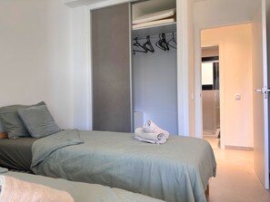 A bedroom with a bed, a closet with hanging clothes, and a bathroom visible through an open door.