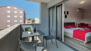 Un balcón con mesa y sillas, una cama con ropa de cama roja, y vista a la ciudad.