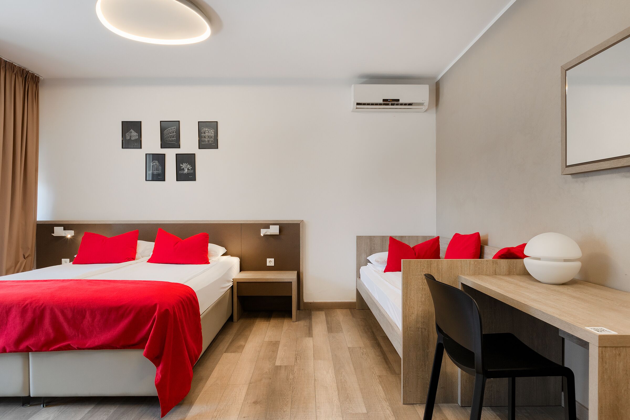 Une chambre d’hôtel moderne équipée d’un lit, d’une table de chevet, d’un bureau, d’une chaise et d’un climatiseur fixé au mur.