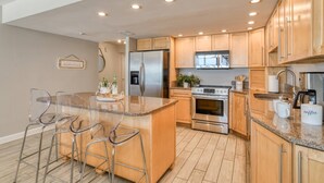 A modern kitchen with wooden cabinets, stainless steel appliances, a granite countertop, and bar stools. - Sand Dollar 306 (St. Augustine)