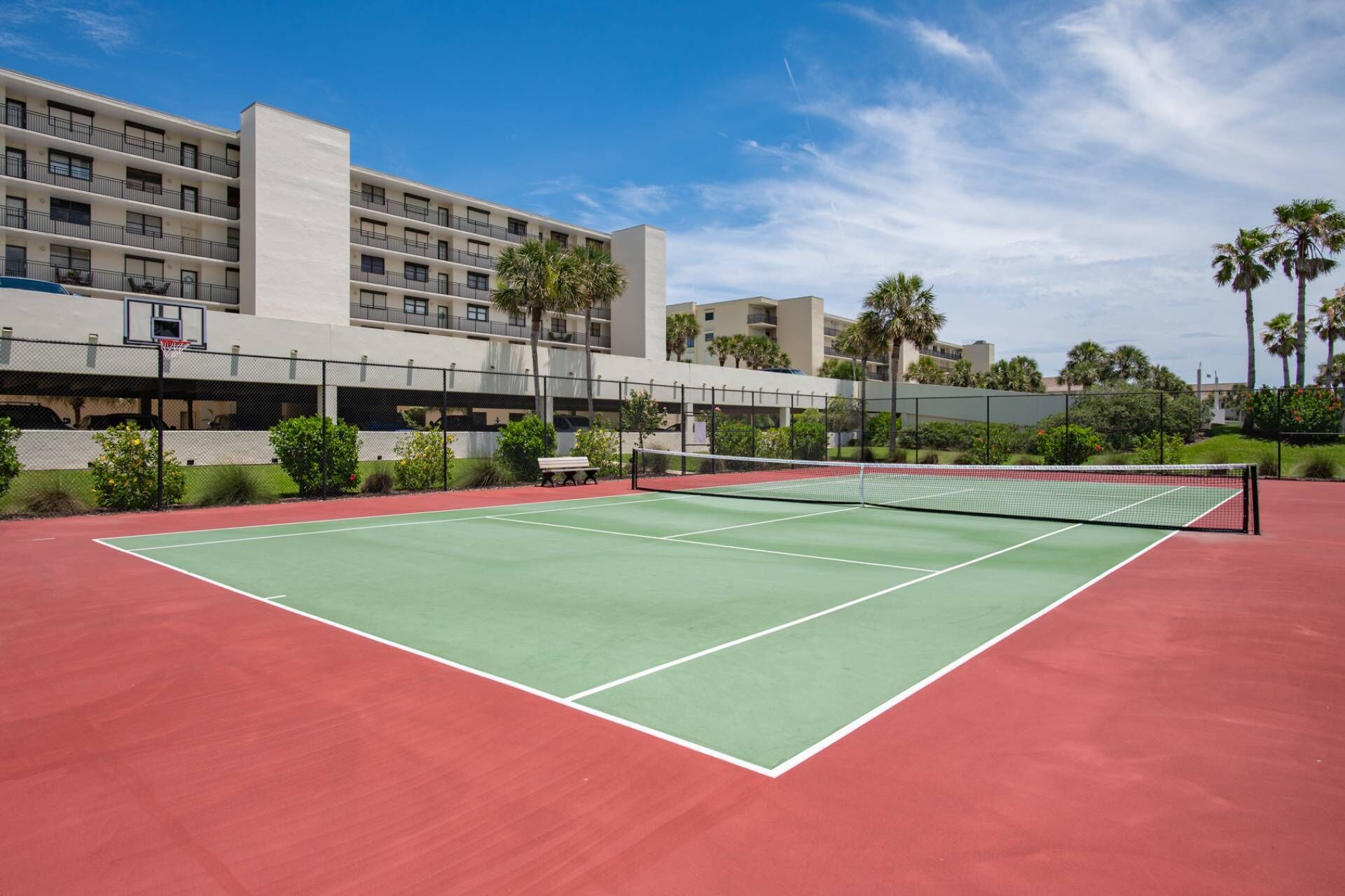 Un court de tennis en plein air, doté d’un filet, entouré d’une clôture et bordé de palmiers.
