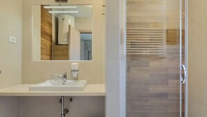 Un baño moderno con un espejo grande, un lavamanos y una cabina de ducha de vidrio.