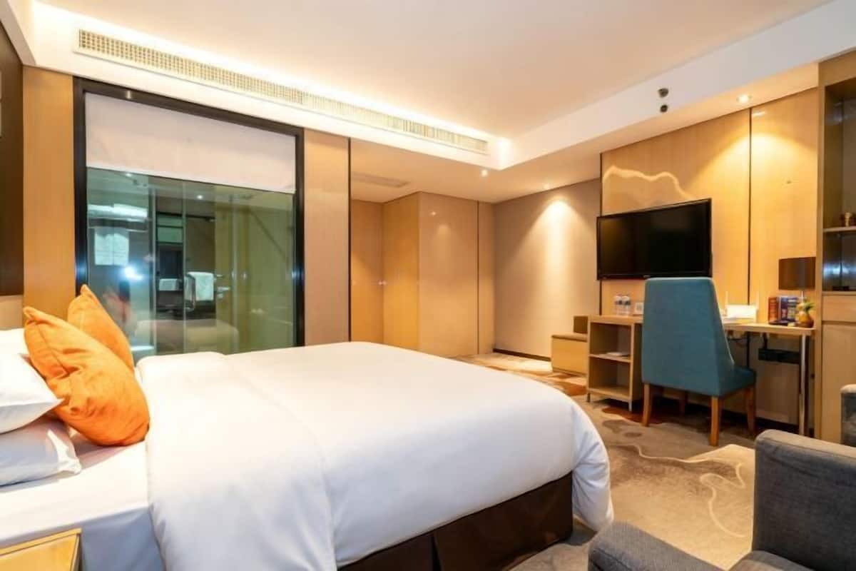 Une chambre d’hôtel équipée d’un lit, d’un bureau, d’une chaise, d’une télévision et d’une cloison en verre.