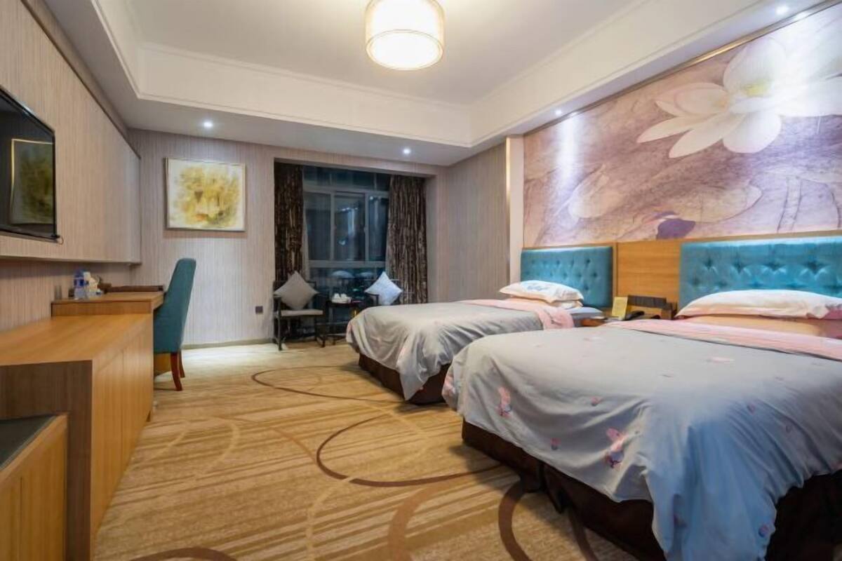 Une chambre d’hôtel avec deux lits, un bureau, une chaise et un grand décor mural représentant des motifs floraux.