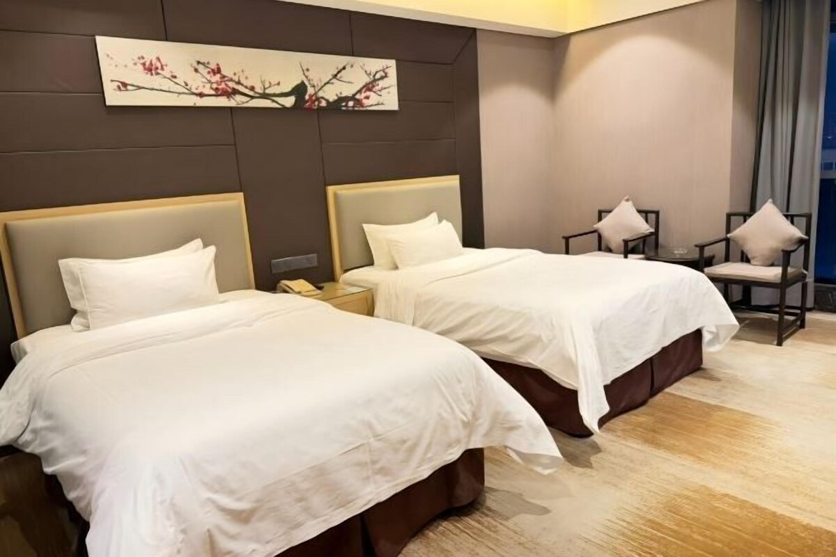 Habitación de hotel con dos camas, una mesita de noche, una silla y un cuadro en la pared.