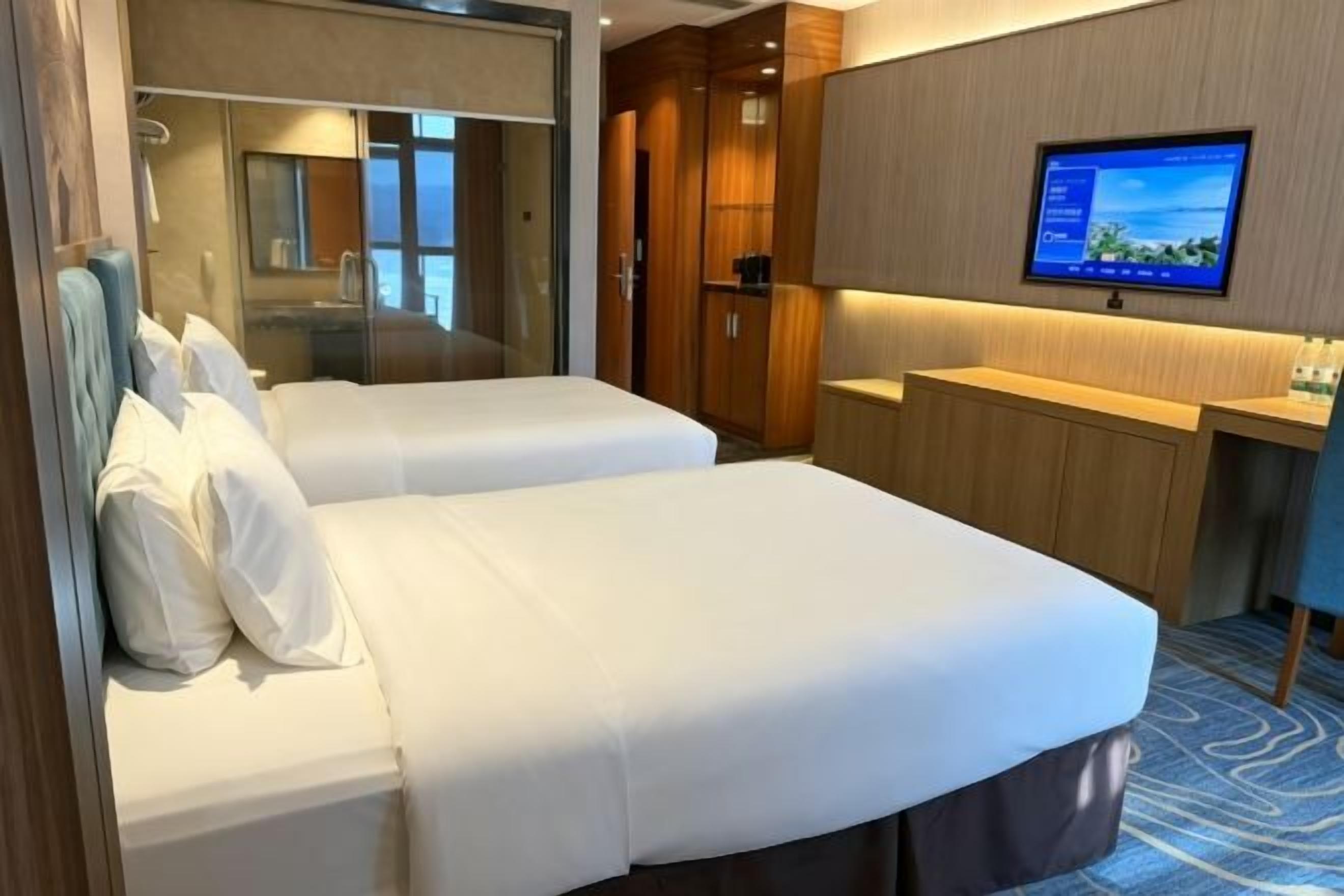 A hotel room with two beds, a TV, a mirror, and a wardrobe.