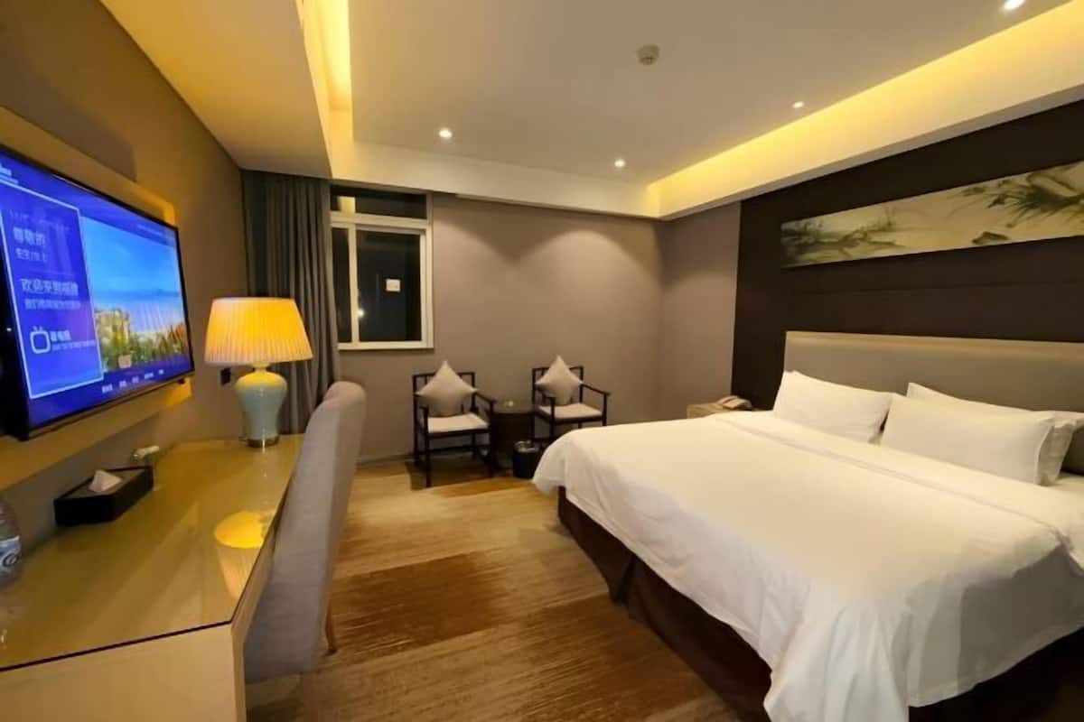 Une chambre d’hôtel avec un grand lit, un bureau avec une télévision, une lampe et deux chaises.