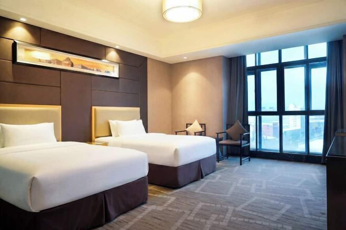Une chambre d’hôtel avec deux lits, un bureau, une chaise et une grande fenêtre.