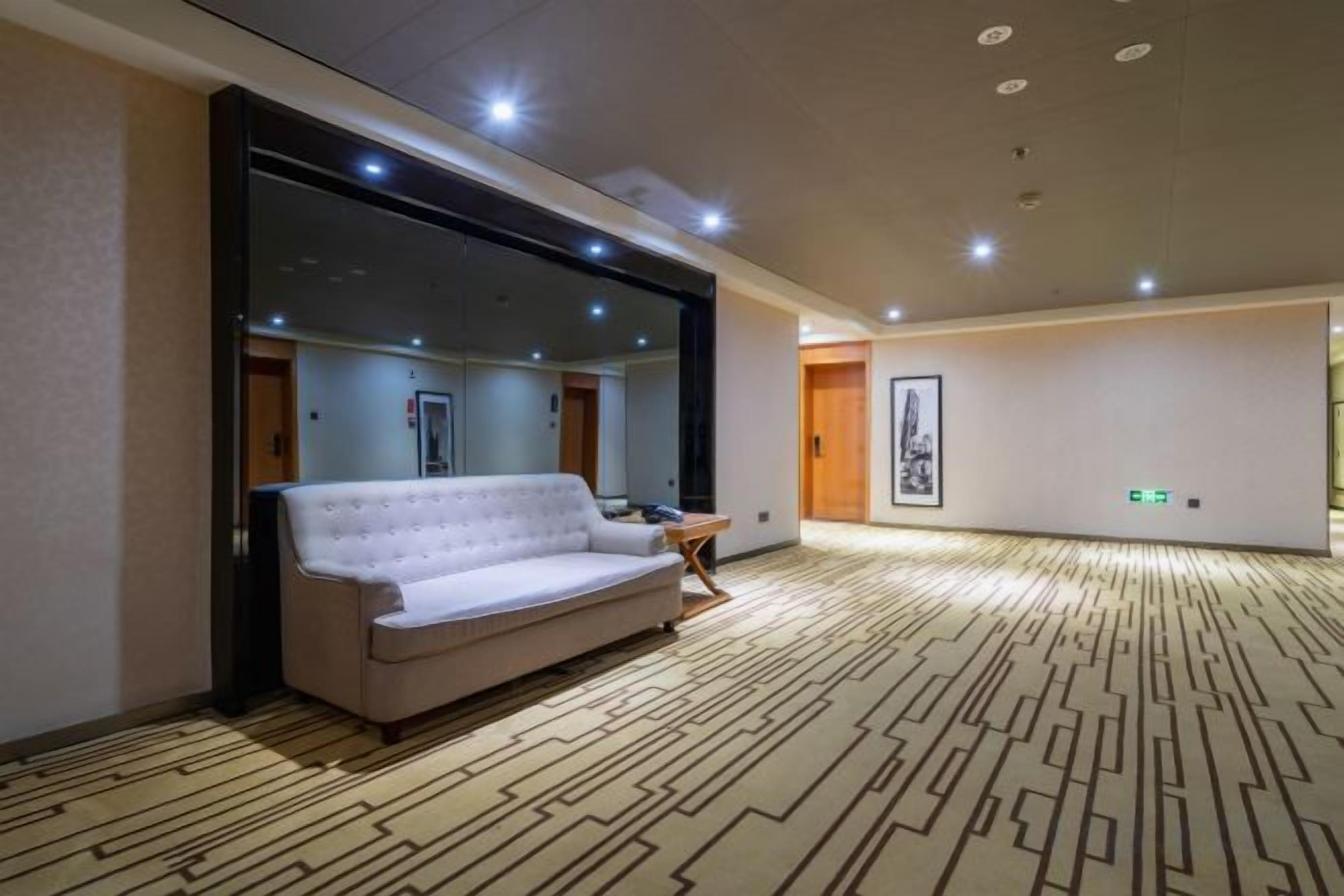 A hotel room with a large mirror, a sofa, a small table, and a patterned carpet.