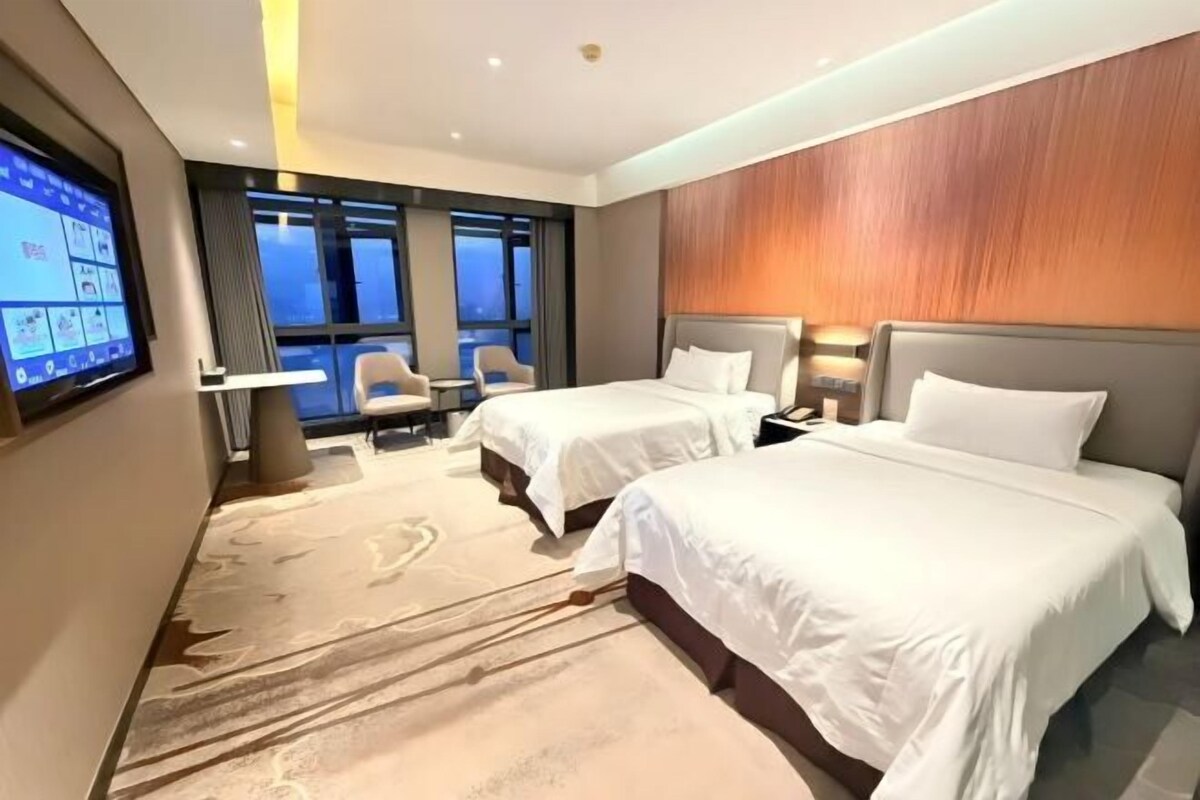 Habitación de hotel con dos camas, televisión, escritorio y vistas a la ciudad.