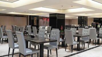 Un comedor de hotel con varias mesas y sillas, una pantalla grande y un diseño de interiores moderno.