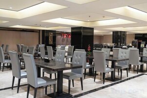 A hotel dining area with multiple tables and chairs, a large screen, and a modern interior design.