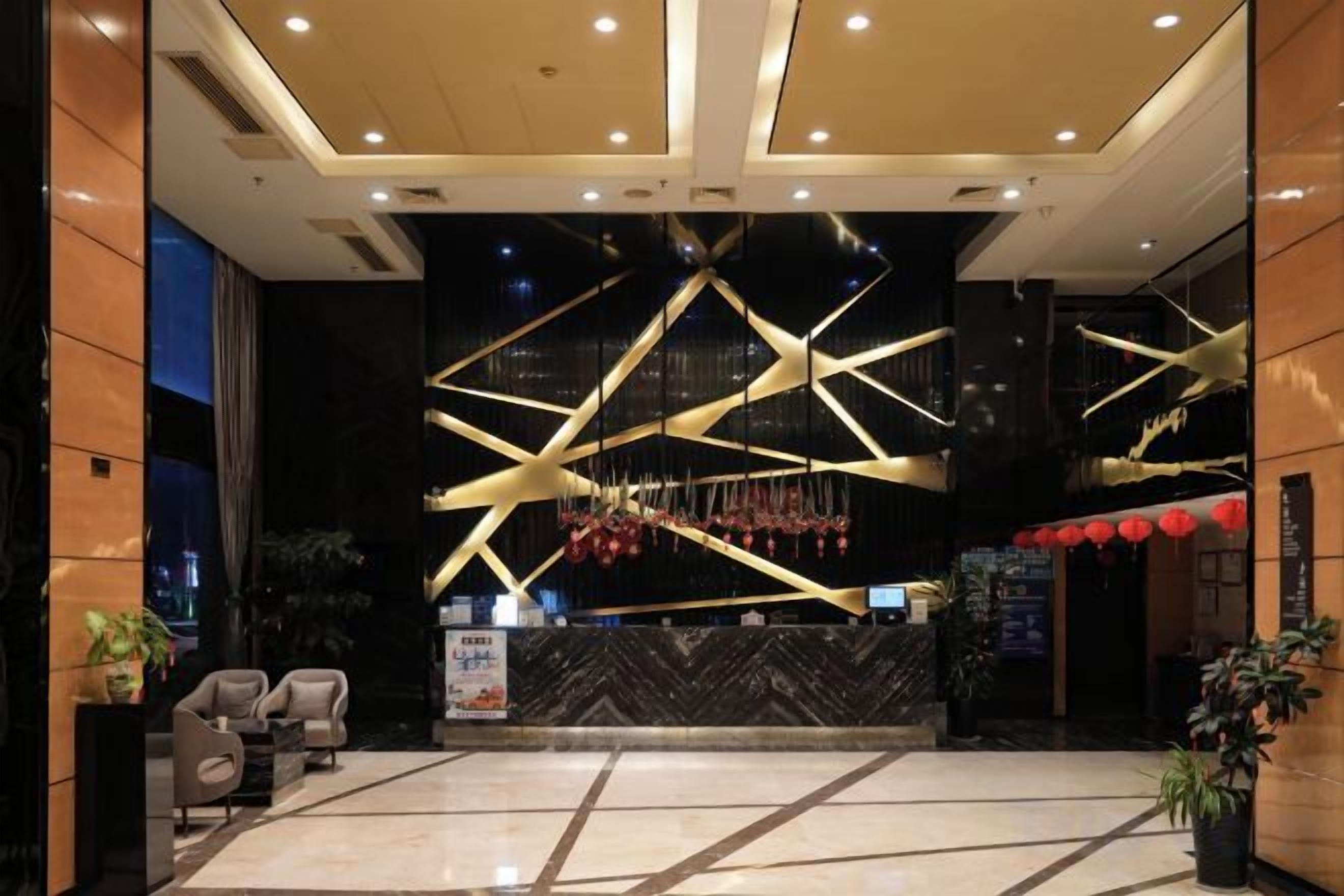 A hotel lobby with a reception desk, seating area, and a modern chandelier.