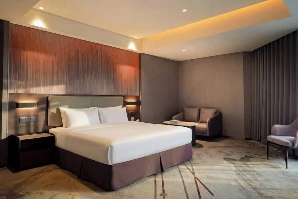 Une chambre d’hôtel moderne dotée d’un grand lit, d’un coin salon avec un canapé et des fauteuils, et d’un panneau mural décoratif.