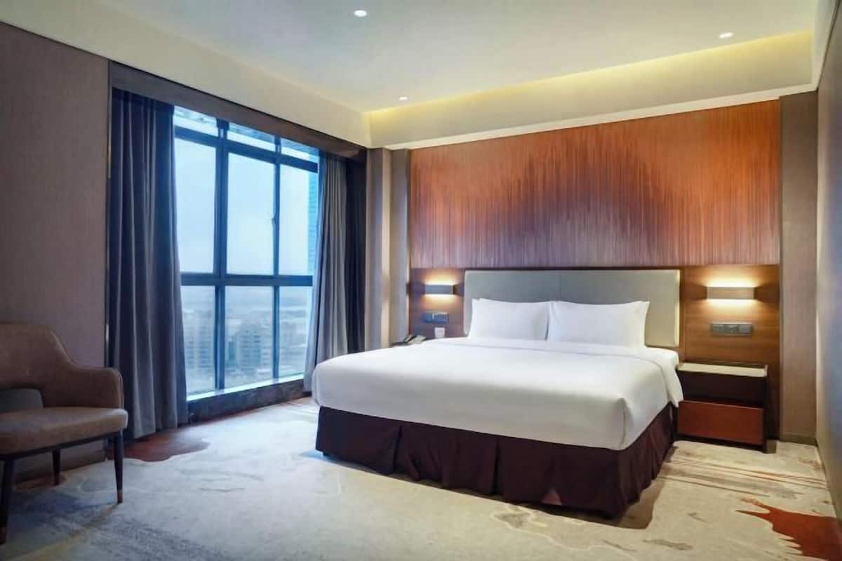 Une chambre d’hôtel avec un grand lit, une chaise, une table de chevet et une vue sur la ville par la fenêtre.