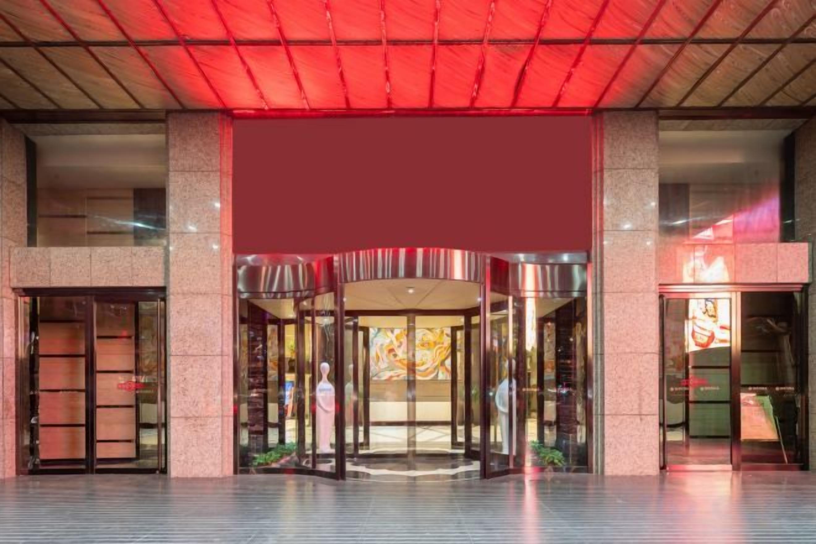 A hotel entrance with a revolving door, a glass facade, and a red awning.